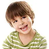 A young child with brown hair smiles brightly, wearing a green striped shirt. The background is plain white, conveying a cheerful and playful mood.
